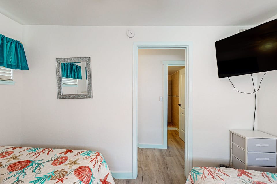 Relax in this cozy coastal guest bedroom with beach-themed décor, comfortable beds, and a TV for downtime. A welcoming retreat to recharge after a fun-filled day enjoying your seaside vacation.