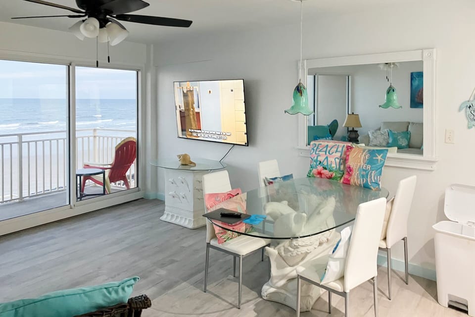 Stylish oceanfront dining and living space featuring glass doors, coastal décor, and sweeping beach views. Enjoy meals and relaxation with the sound of waves, creating the perfect beach stay and seaside vacation experience.