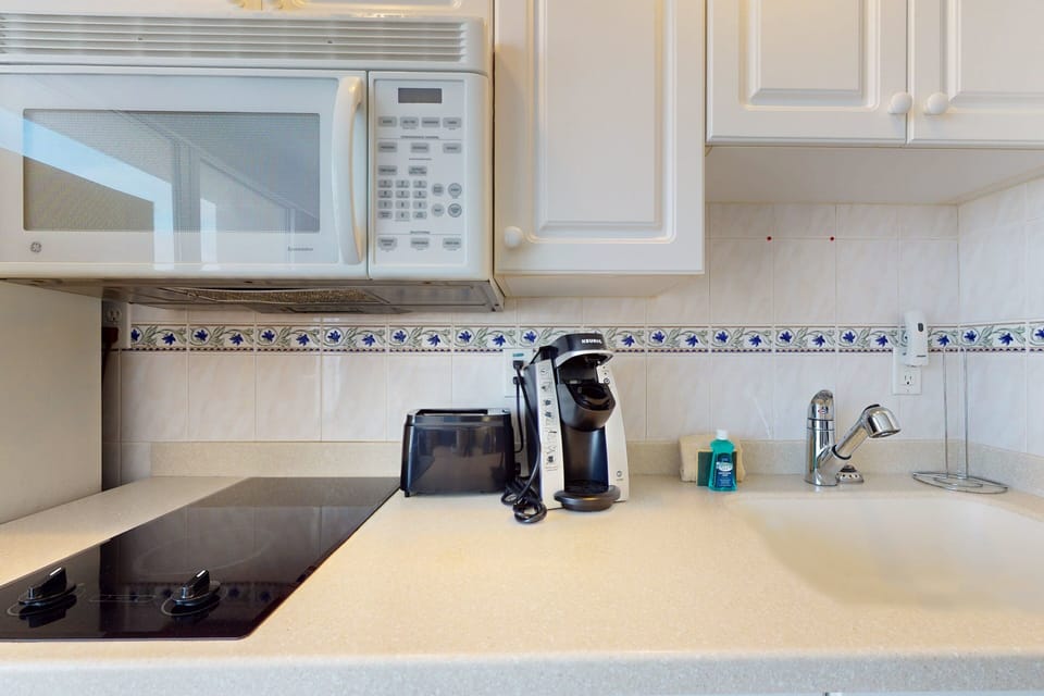 Enjoy the comfort of a well-equipped kitchenette during your beach stay, featuring a microwave, cooktop, coffee maker, and spacious counter space—perfect for easy meals between ocean adventures.
