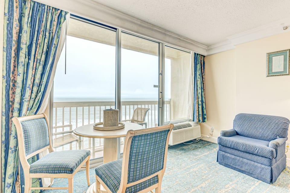Relax in this cozy oceanfront nook featuring comfy seating, a dining table, and floor-to-ceiling windows showcasing breathtaking beach views—perfect for enjoying your peaceful coastal stay.