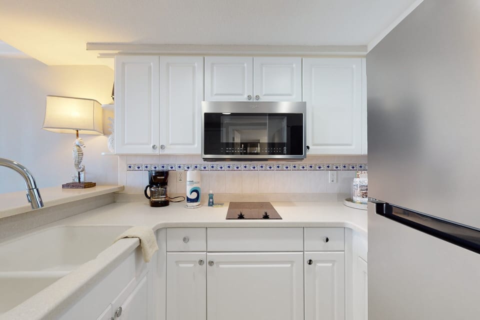 Fresh, beach-ready kitchenette featuring modern appliances, crisp white cabinetry, and ocean-inspired décor—perfect for preparing quick meals during your relaxing seaside stay.