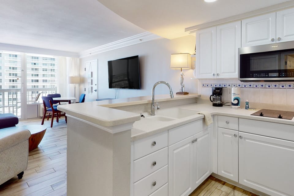 Enjoy a breezy beach-stay vibe in this open kitchen and living area, featuring crisp white cabinetry, modern appliances, and balcony views. Perfect for relaxing after a day on the sand.