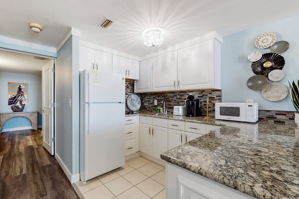 Enjoy this fully equipped kitchen featuring granite counters, crisp white cabinetry, and coastal décor—perfect for preparing meals during your relaxing beach stay.