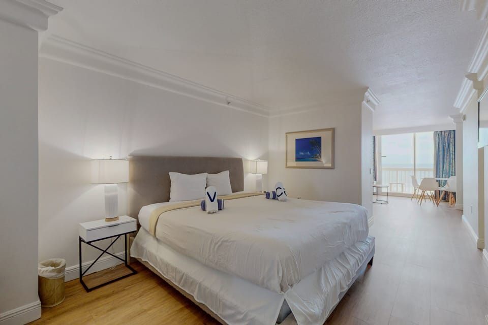 Relax in this stylish beach-stay suite featuring a plush king bed, clean modern décor, and bright natural light leading to stunning ocean views—perfect for a peaceful coastal retreat.