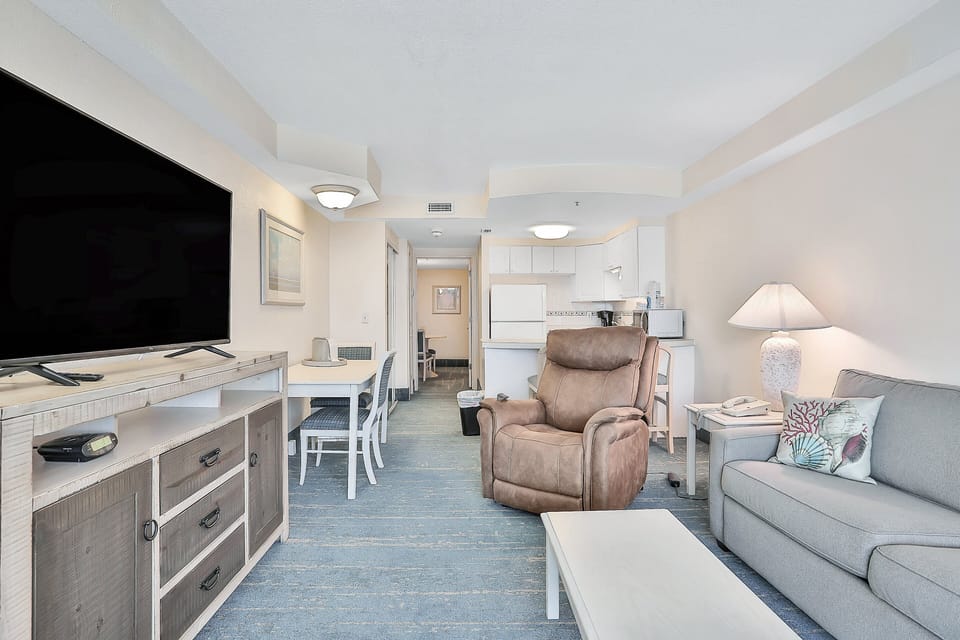 Relax in this beach-style living space featuring cozy seating, a large TV, and easy access to the kitchen and dining area—perfect for unwinding after a sun-soaked day by the shore.