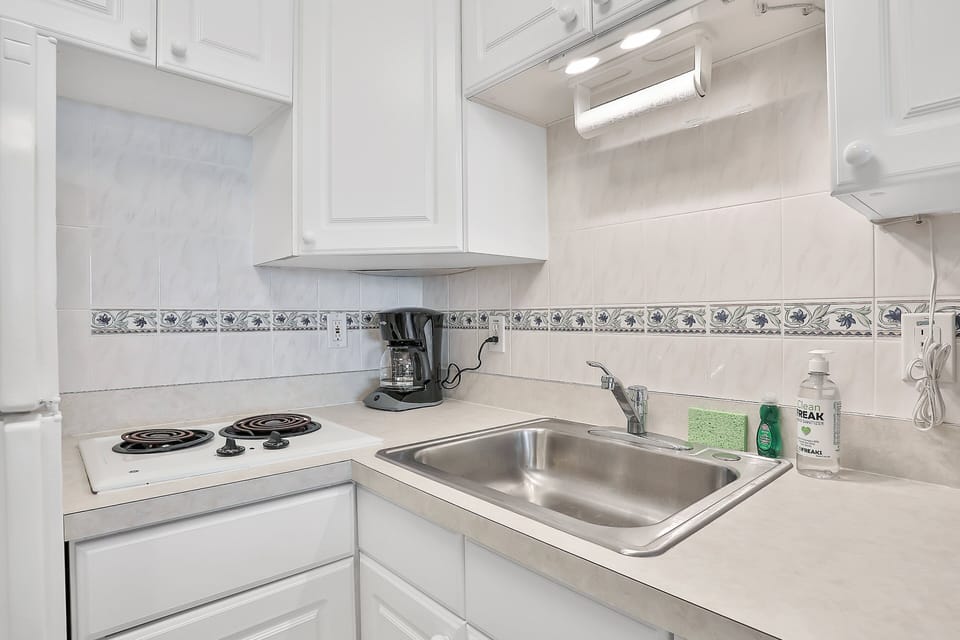 Compact beachside kitchenette with bright white cabinetry, cooktop, and essentials for quick meals during your coastal stay. Perfect for enjoying simple bites before heading back to the ocean.