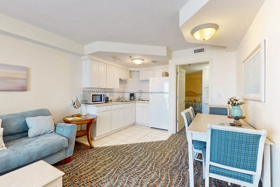 Enjoy this inviting beach stay layout featuring a comfy sofa, full kitchenette, and spacious dining area—perfect for relaxing and sharing meals after a sun-filled day by the ocean.
