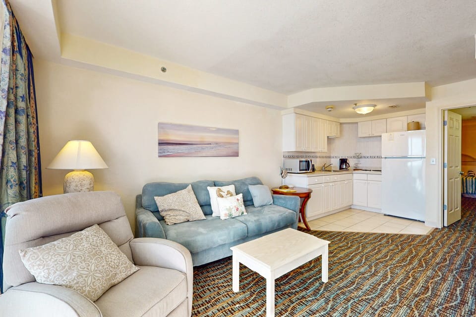 Enjoy a relaxing beach stay in this bright living space featuring comfy seating, coastal décor, and a full kitchenette—perfect for unwinding after a sun-filled day by the ocean.