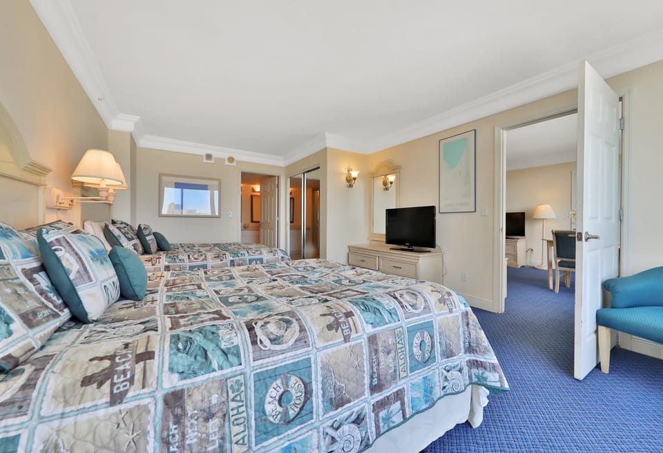 Relax in this inviting beach-stay bedroom featuring two plush beds with coastal décor, a TV, and easy access to the living area—perfect for a comfortable seaside retreat.
