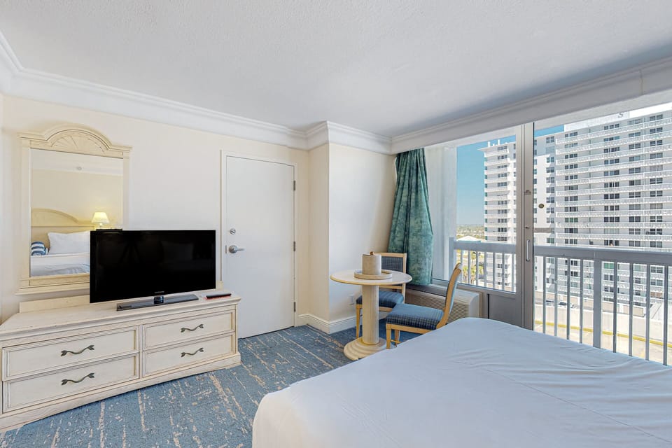 Sunlit room with cozy seating, TV, and balcony access overlooking the coastline—perfect for relaxing after a fun-filled beach stay.