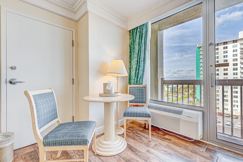 Enjoy a relaxing beach stay with this bright seating nook, featuring comfy chairs and large windows showcasing vibrant city and shoreline views. Perfect for morning coffee or unwinding after a day in the sun.
