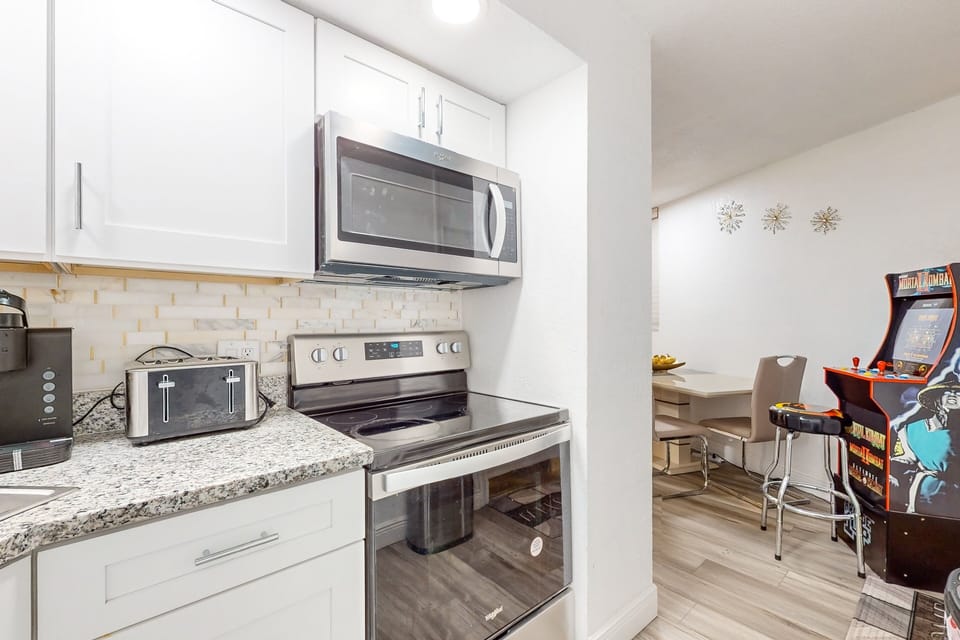 Modern coastal kitchen with stainless appliances opens to a casual dining space. Perfect for easy meals and family time during your relaxing beach stay near sun, sand, and ocean fun.