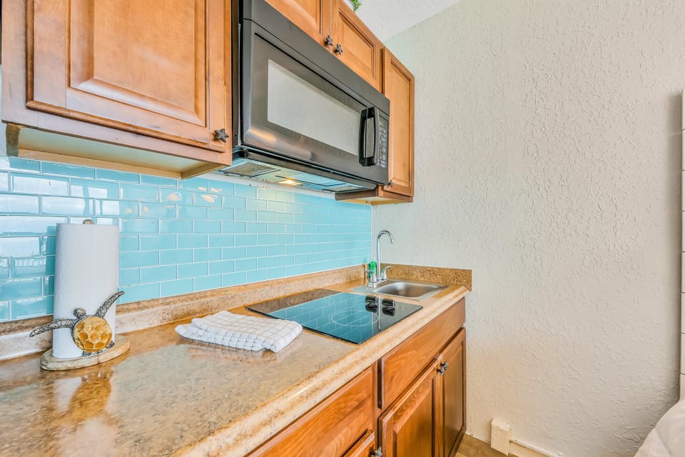 Compact beach-inspired kitchenette with cooktop, microwave, and coastal tile backsplash. Ideal for a relaxed beach stay, offering everything you need for light meals after a day by the ocean.