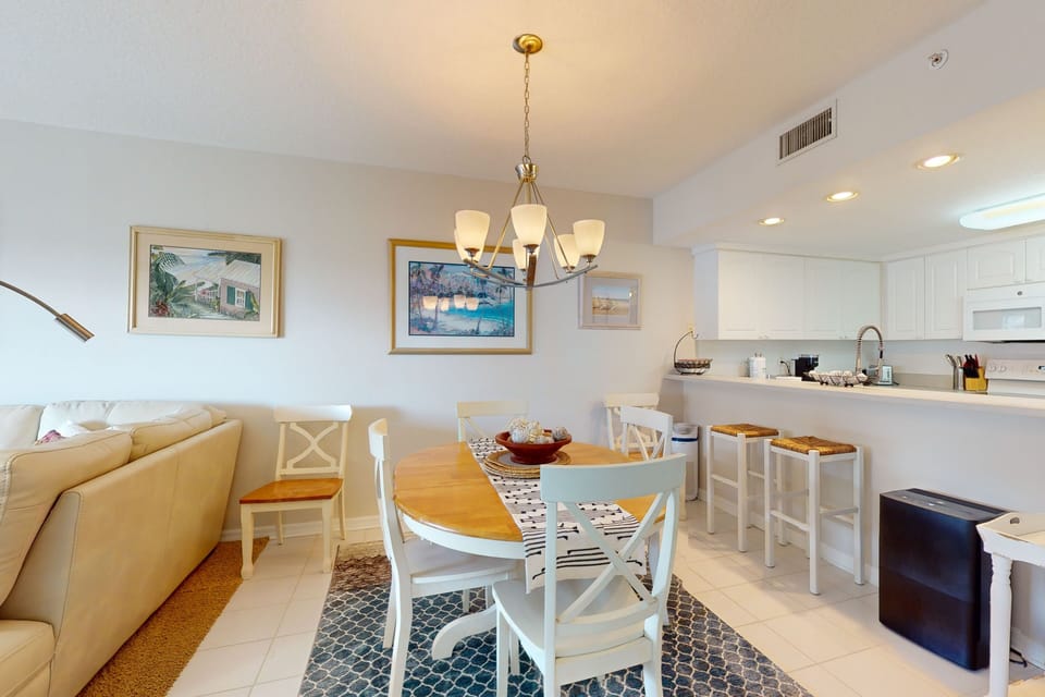 Inviting open dining space with coastal décor, breakfast bar seating, and bright kitchen flow. Ideal for easy meals and relaxing moments during your beach stay, offering comfort and convenience after days spent by the shore.