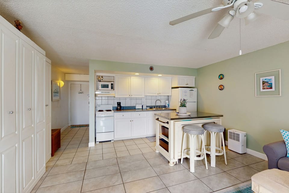 This open-concept kitchen and living area is ideal for a relaxing beach stay, featuring island seating, bright coastal décor, and plenty of space to unwind after a fun-filled day at the beach.