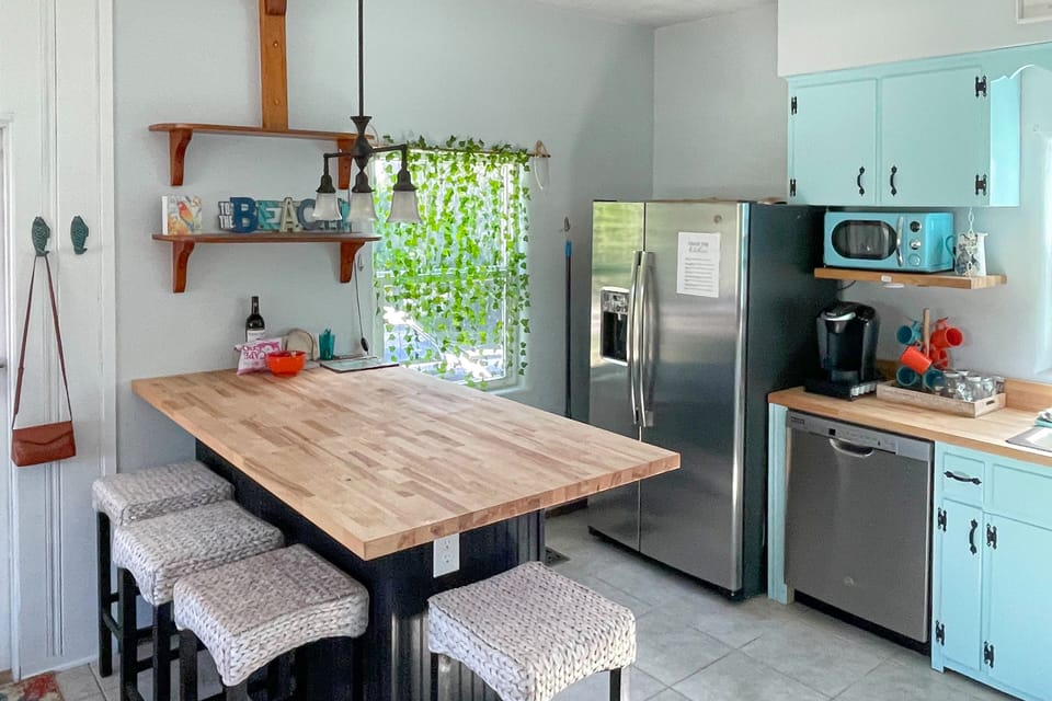 Charming beach-style kitchen featuring a spacious butcher-block counter, cozy bar seating, and aqua cabinets. Perfect for prepping seaside meals during your relaxing beach stay.