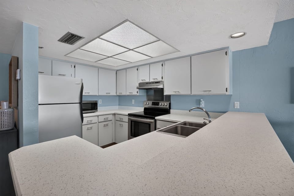 Prepare meals with ease in this bright, spacious kitchen featuring ample counter space, full-size appliances, and a convenient breakfast bar—perfect for casual dining and refreshments during your beach stay.