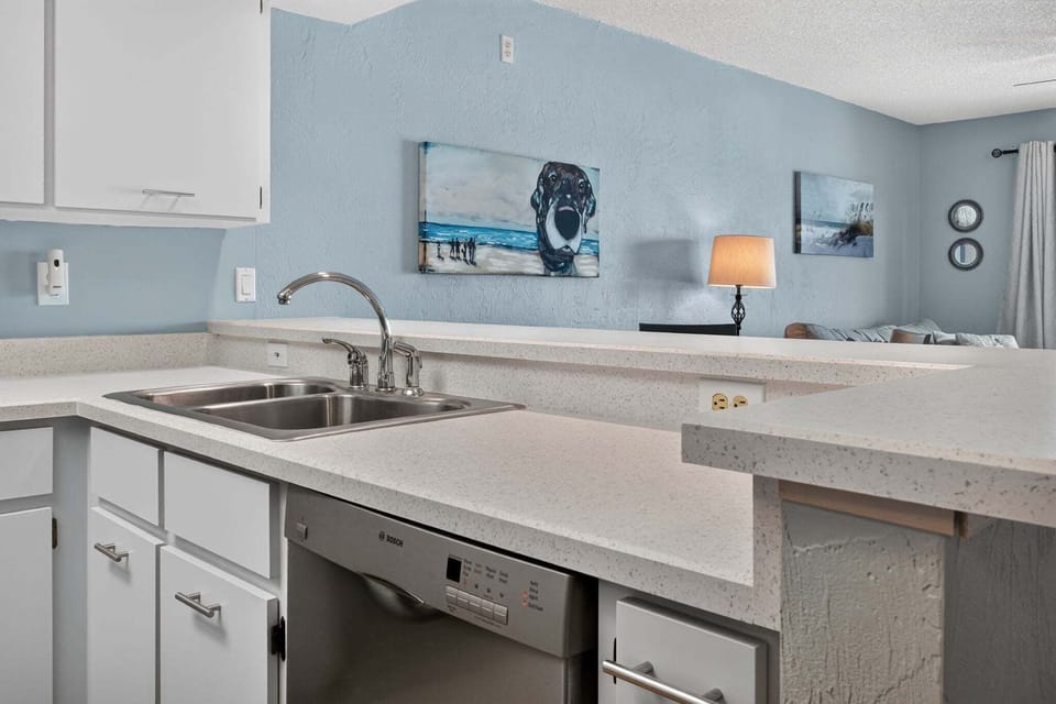 Enjoy the convenience of this open kitchen featuring generous counter space, a double sink, dishwasher, and breakfast bar overlooking the living area—perfect for easy meals and snacks during your beach stay.