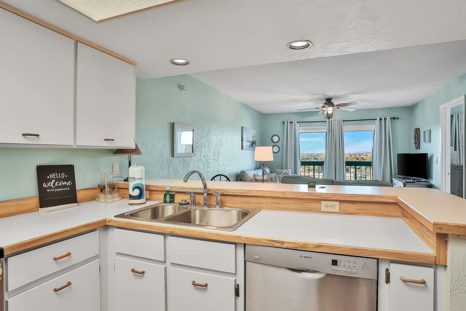 This bright coastal kitchen features ample counter space and an open layout overlooking the living room and balcony. Perfect for a beach stay, it makes cooking, dining, and relaxing easy after days by the shore.