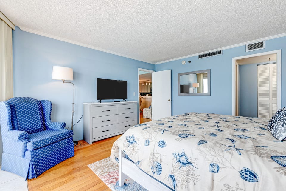 Airy beachside bedroom with comfortable bedding, cozy seating, and coastal décor. Enjoy a peaceful retreat with space to relax after long days soaking up the sun during your beach stay.