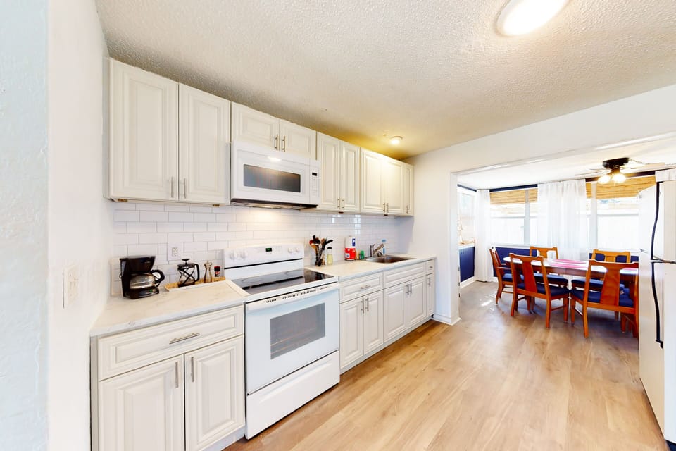 Enjoy home-cooked meals in this bright beach stay kitchen featuring white cabinetry, full-size appliances, and ample counter space. Open to the dining area, it's perfect for gathering after a relaxing day at the beach.