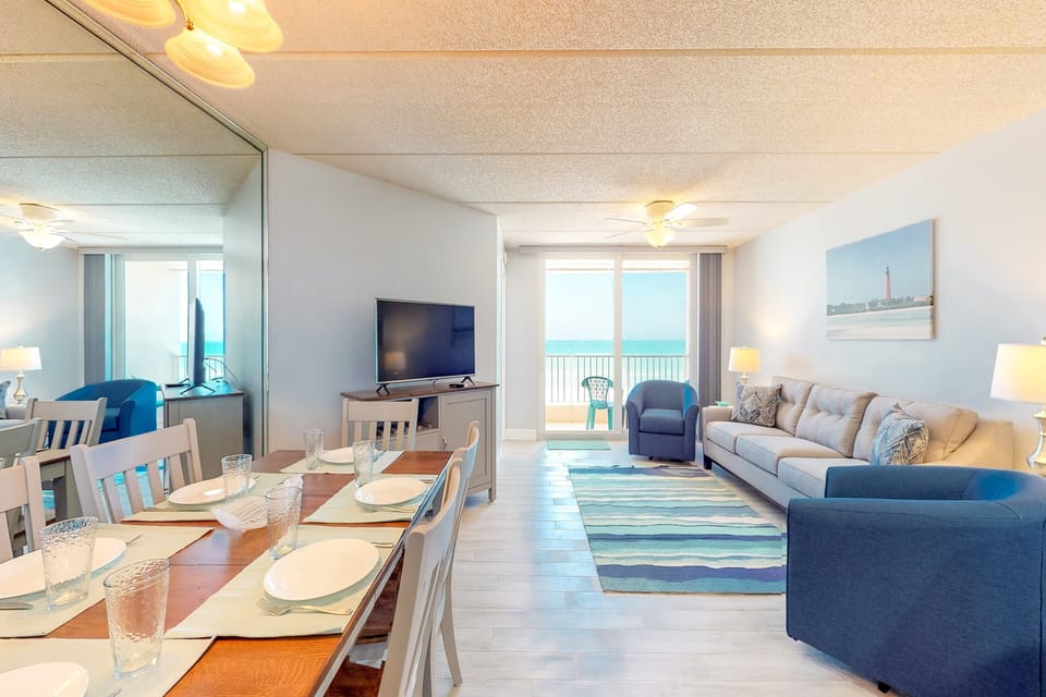 This bright beach stay space features a spacious dining table and cozy living room with direct balcony access and stunning ocean views—perfect for relaxing and enjoying meals by the shore.