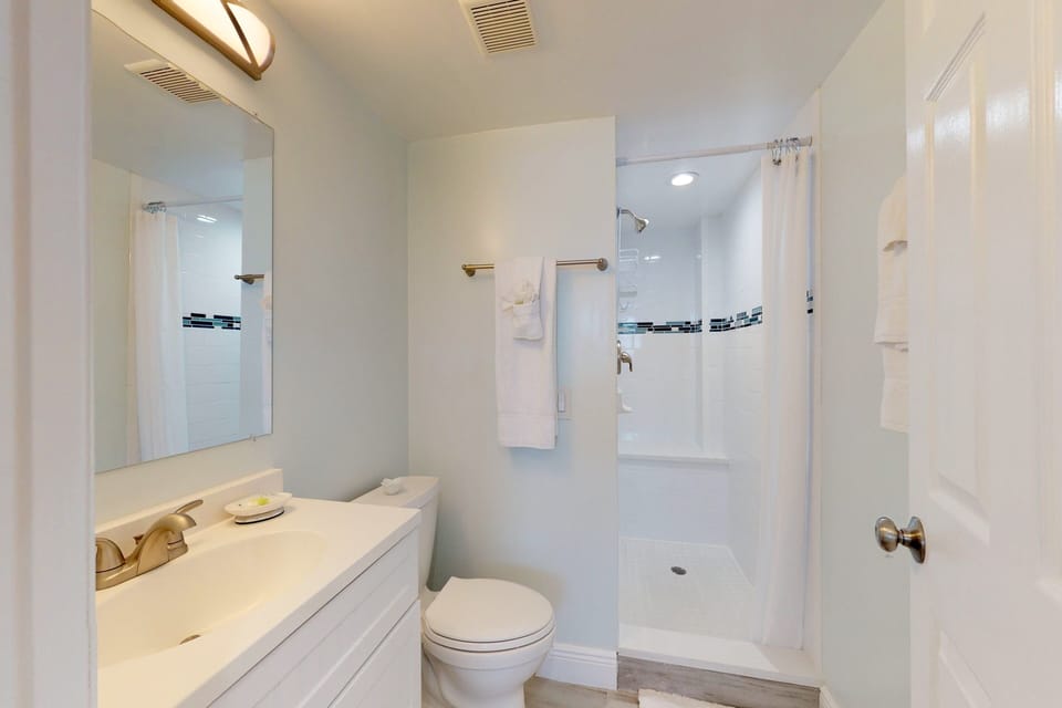 This bright beach stay bathroom features a clean vanity, walk-in shower, and crisp coastal touches—offering a refreshing space to unwind after a day by the ocean.