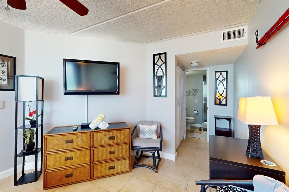 Bright beach-inspired bedroom featuring a flat-screen TV, dresser, and direct access to a private bathroom—perfect for a relaxing oceanfront stay.