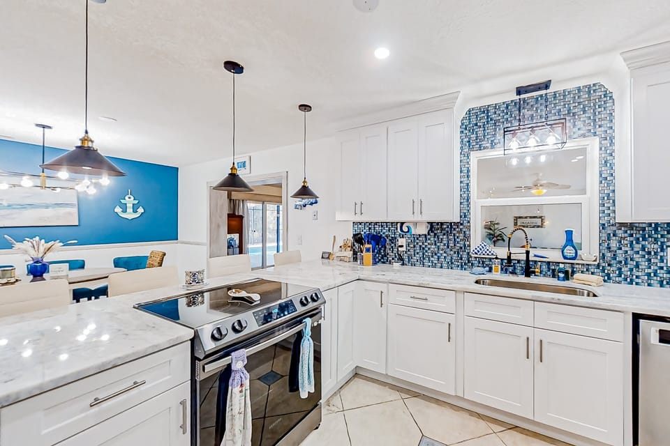 Bright, beach-inspired kitchen with marble counters, modern appliances, and nautical accents—perfect for cooking after a sun-soaked beach stay. Open layout flows into the dining area for easy vacation gatherings.
