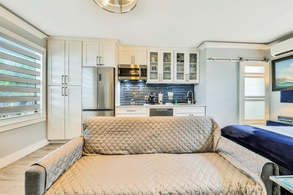 Relax in this inviting beach stay living area featuring comfortable seating, coastal tones, and a view of the modern kitchenette. A perfect spot to unwind after a sun-filled day by the beach.