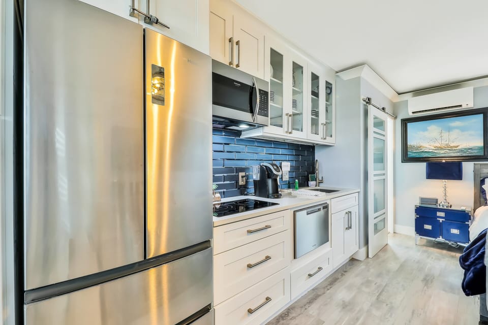 This sleek beach stay kitchenette features stainless steel appliances, coastal blue backsplash, and modern cabinetry. Perfect for preparing meals after a day at the beach while enjoying comfort and seaside style.