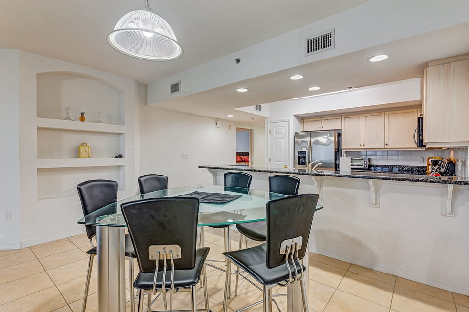 Enjoy meals together in this bright dining area with a glass table and open kitchen. Perfect for a relaxing beach stay, this coastal condo offers modern appliances and an inviting space to gather after the beach.