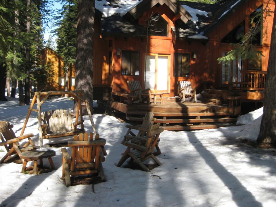 The charming exterior of the Northstar home is surrounded by snow-covered grounds, featuring inviting wooden seating areas perfect for enjoying the serene forest backdrop.