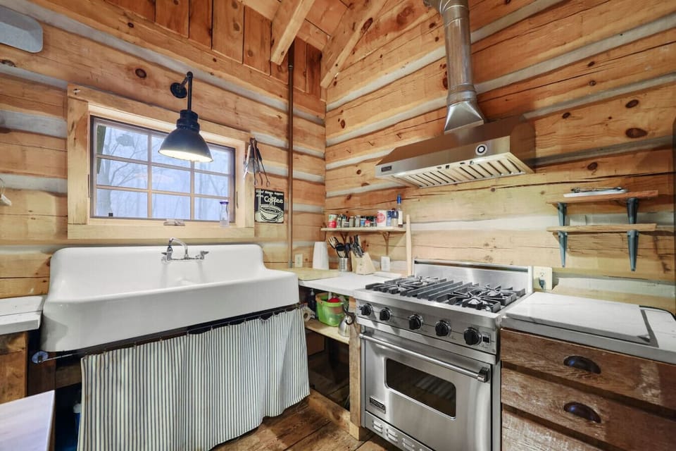 A rustic farmhouse kitchen with a deep porcelain sink, warm wood walls, and a vintage-style pendant light.