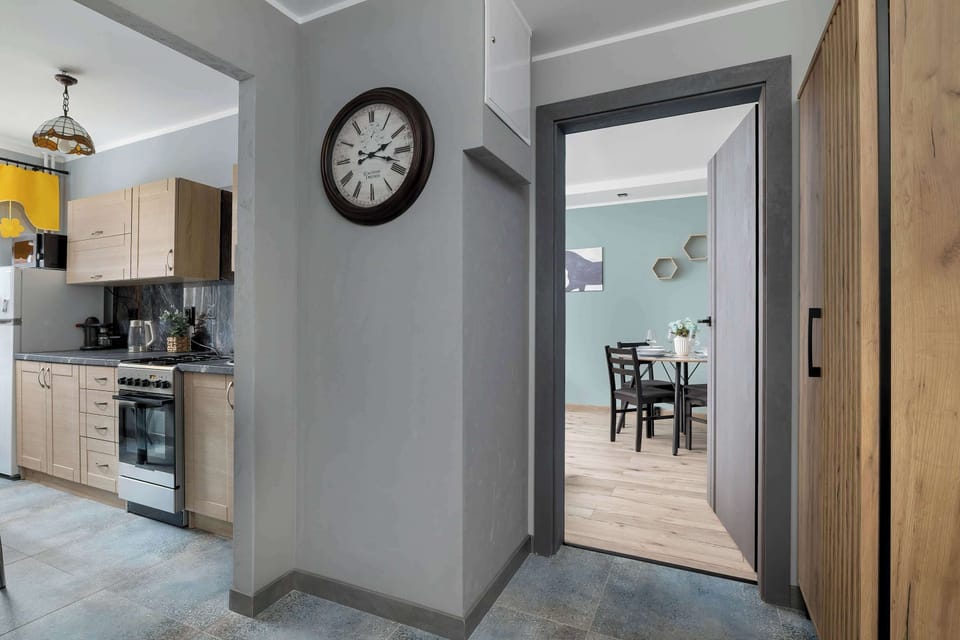 The passage between the kitchen and living room, enhanced by warm lighting and a classic wall clock, guides guests naturally through the home’s inviting layout.
