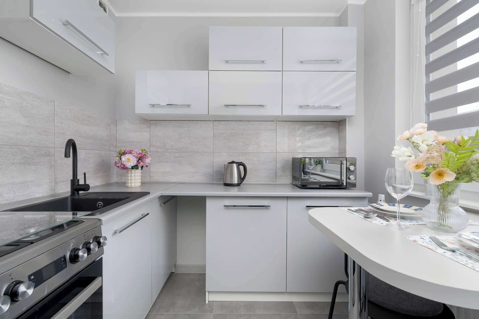 A small kitchen with clean white cabinetry and light countertops. A dining setup in the foreground hints at a cozy meal area. The polished look makes the space feel inviting and organized.