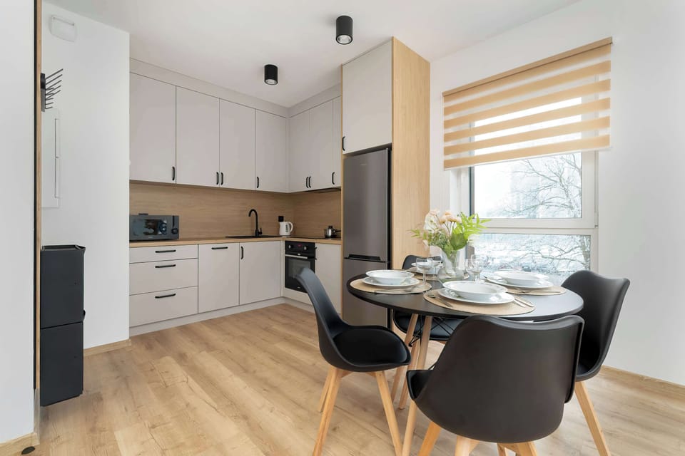 A kitchen with white cabinets, wooden countertops, and a small dining table. Black chairs complement the sleek, modern look.