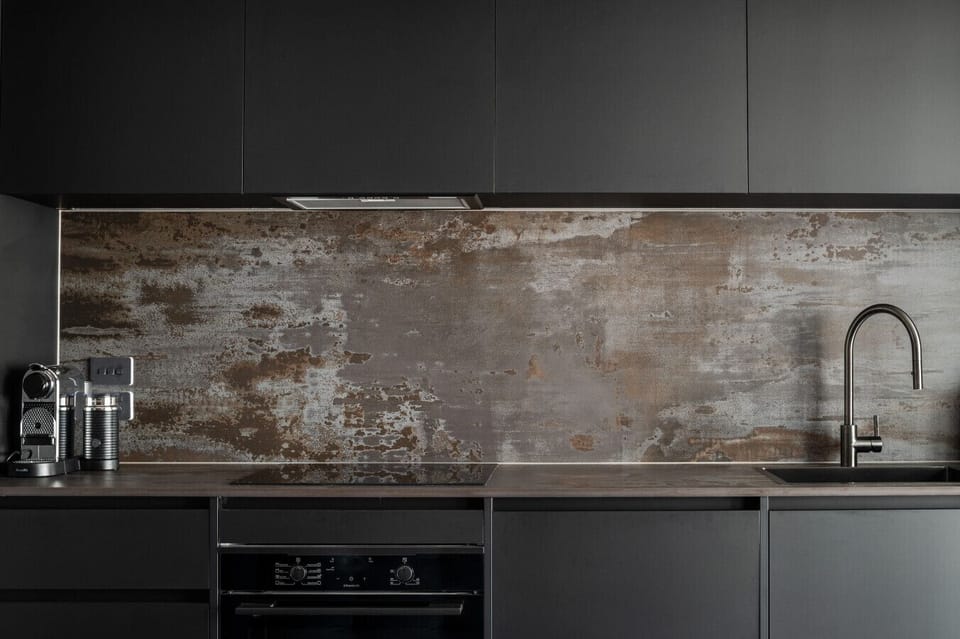 Modern kitchenette with sleek black cabinetry, quality appliances and a striking industrial splashback