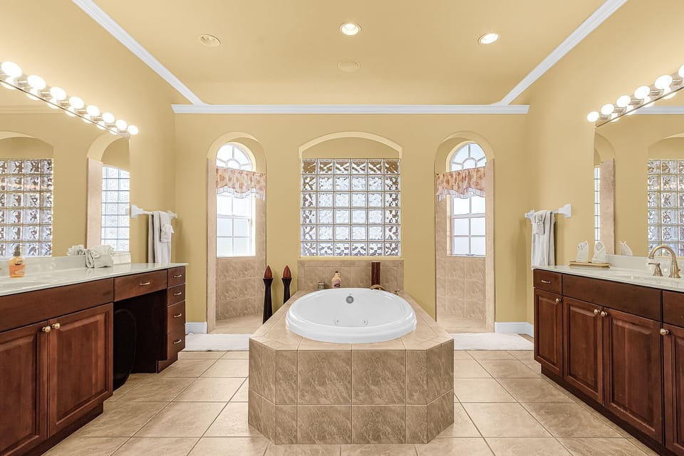 A jetted soaking tub, dual vanities, and arched windows flooding the room with natural light — the primary bath at Villa Aveline is a genuine spa experience.