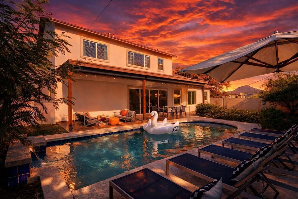 Enjoy a covered patio with outdoor dining for 10, a comfy lounge area with motorized shades, a sparkling pool with loungers and an umbrella, and a grassy area for relaxing or play.
