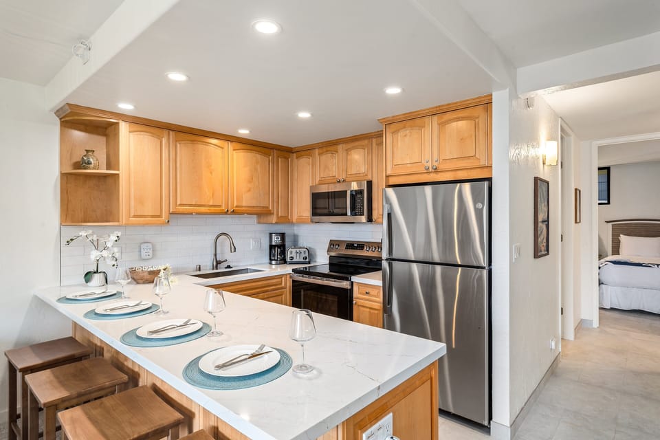 A stylish kitchen awaits—featuring stainless steel appliances, natural wood cabinetry, and a cozy bar area for relaxed dining.