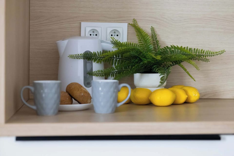 A countertop arrangement with coffee mugs, lemons, and greenery placed decoratively. The wooden background adds warmth to the composition. The small plant brings a fresh, natural touch.