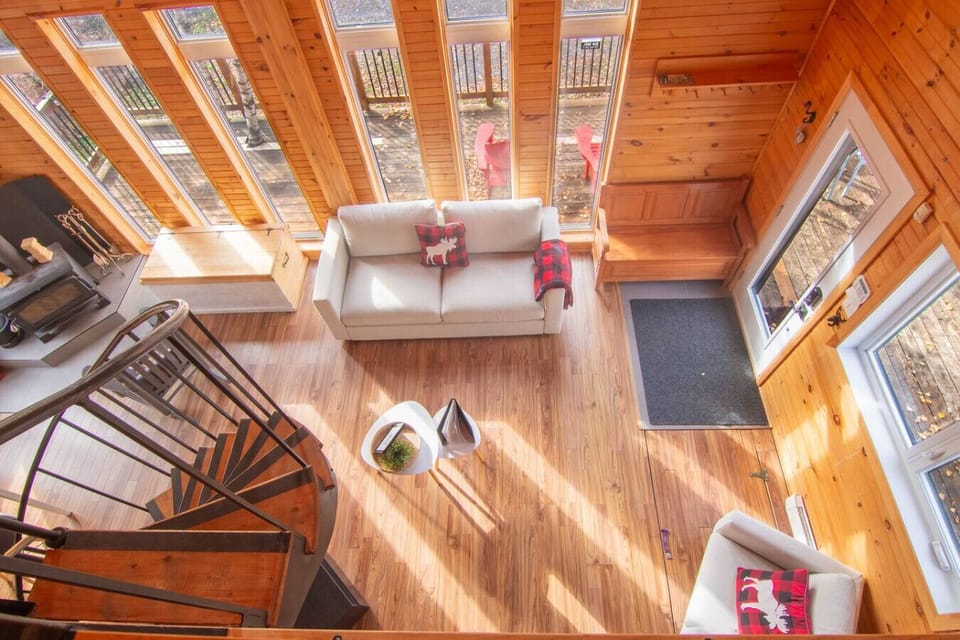 Aerial view of the living room with its large windows overlooking nature. The space is bright, warm and perfectly arranged for enjoying relaxing moments with family.