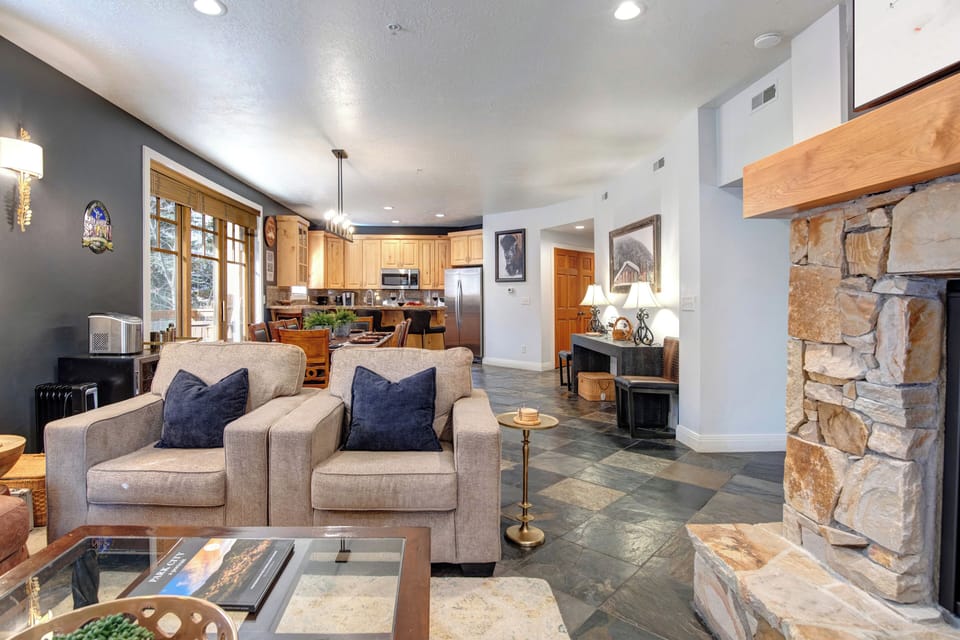 Relax in your spacious open-concept living area featuring a cozy stone fireplace, comfortable seating, and fully equipped kitchen - perfect for unwinding after a day of adventure.