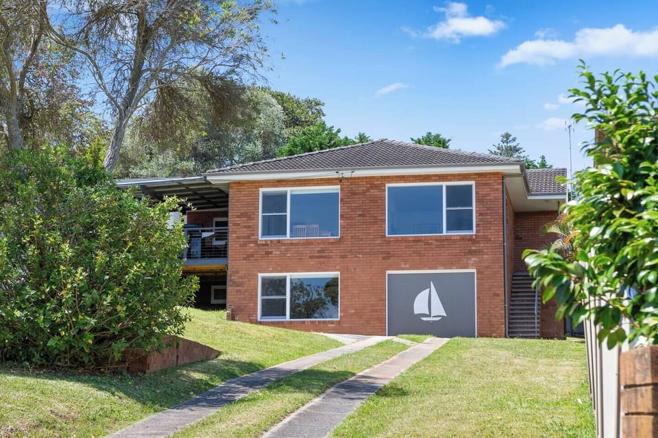 The exterior shows the home’s brick façade, elevated deck and leafy surrounds, offering a quiet, comfortable base near the beach.