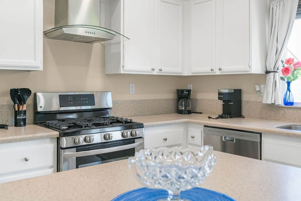 Modern kitchen: stainless appliances, gas range, hood, dishwasher, corner coffee station.