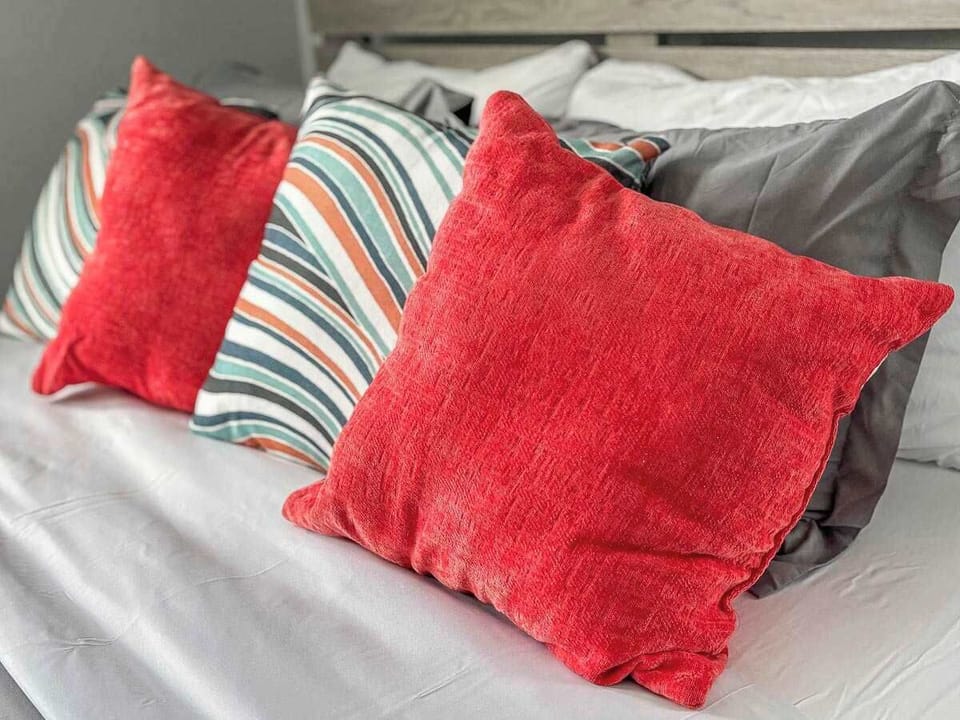 Bright, cheerful pillows add a pop of color to the bed, creating a cozy, inviting space that feels warm, welcoming, and ready for relaxation.