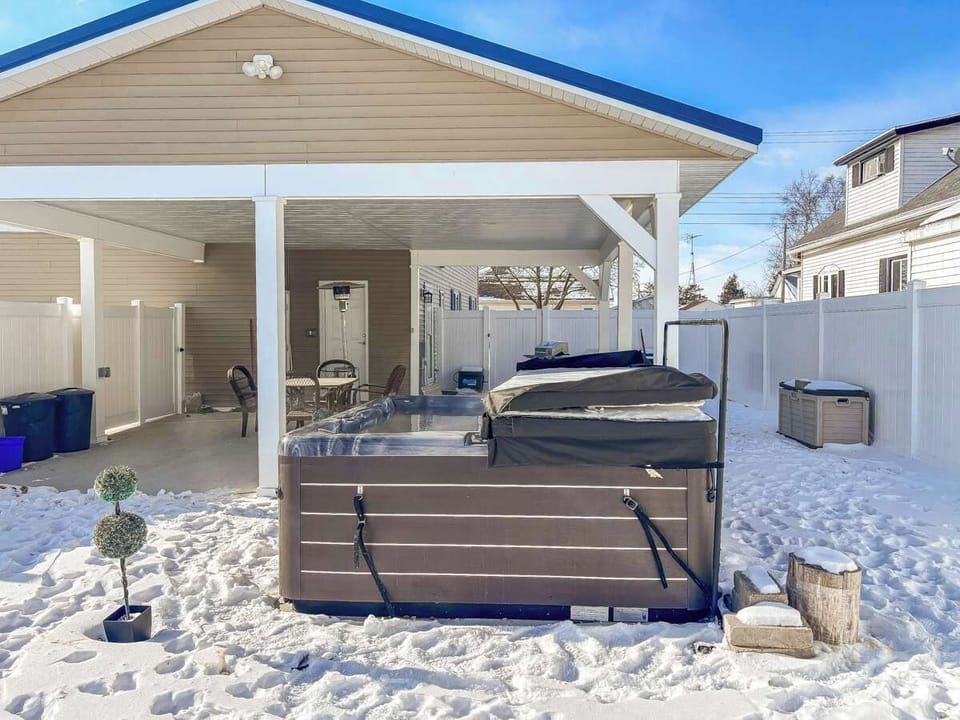 Backyard view showcasing the steaming hot tub and cozy outdoor seating area with a heater. Perfect for relaxing, warming up, and enjoying the fresh air in comfort, no matter the season.