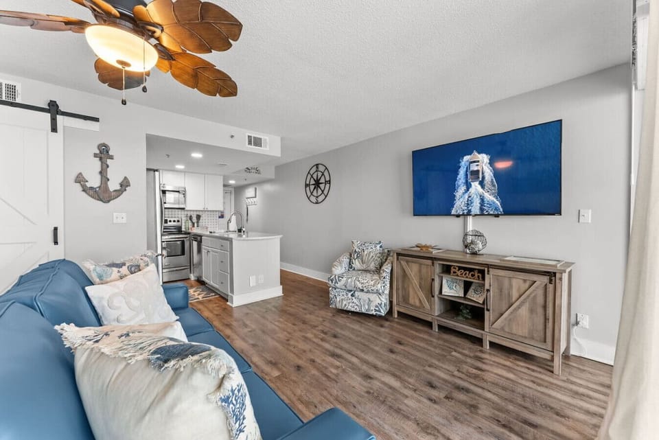 Stylish coastal living room with large Smart TV, comfy seating, and an open layout flowing into the kitchen.