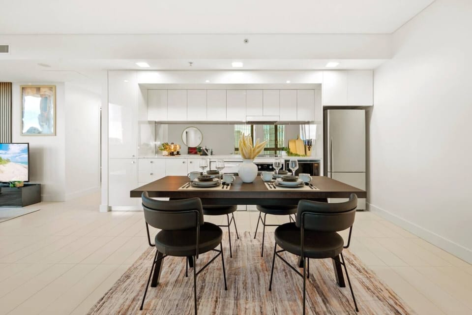 Contemporary dining area with a dark timber table, complete table setting, and a bright open kitchen just steps away.